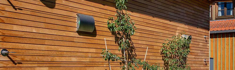 Eine Holzfassade mit Pflanzen und Lüftungsöffnungen, die ein modernes, nachhaltiges Design zeigt. | © Name
