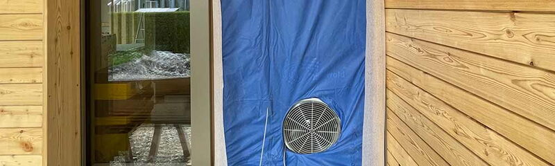Ein Ventilator ist an einer blauen Folie neben einer Holzverkleidung angebracht, um Luftzirkulation zu ermöglichen.