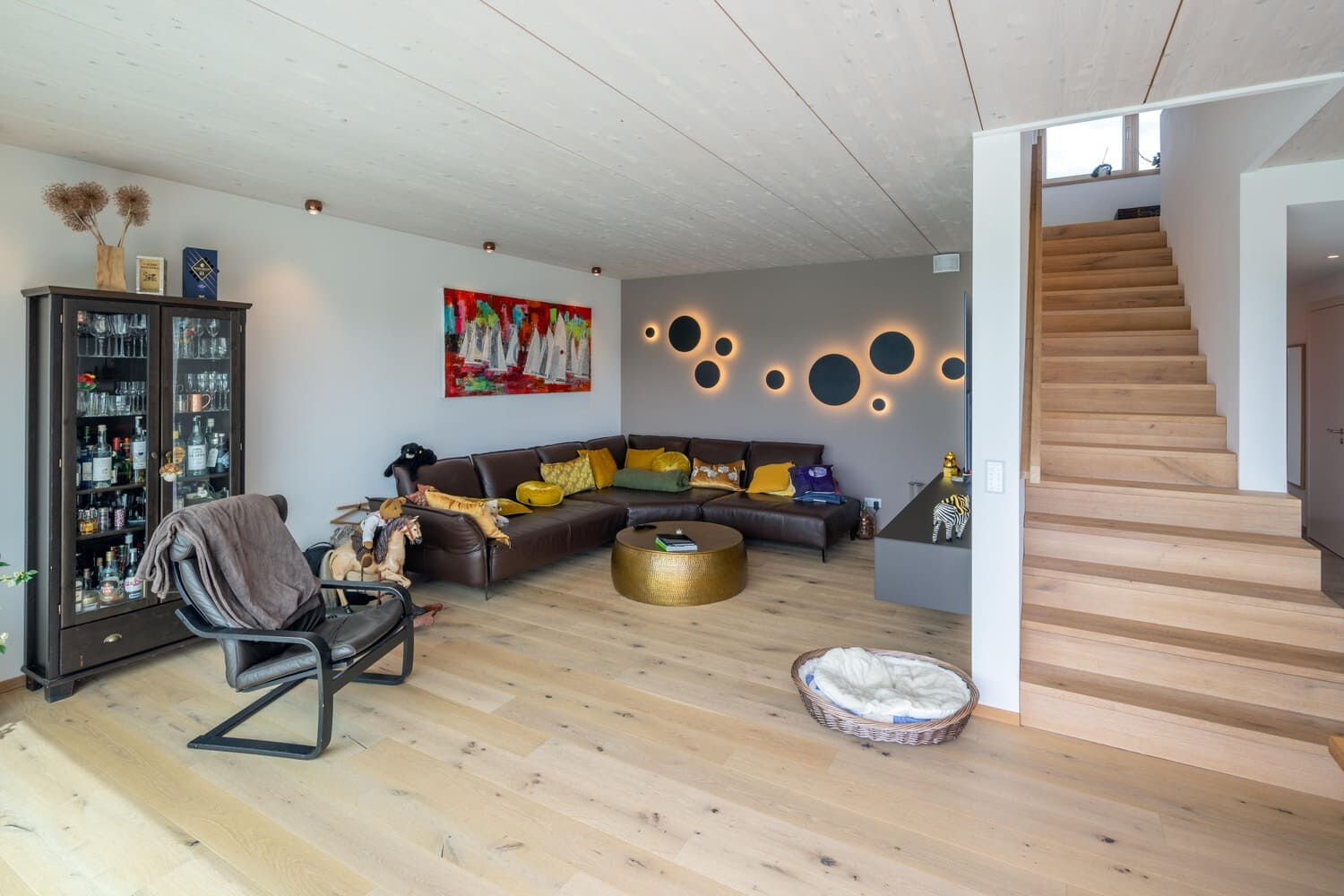 Holzhaus in Weilheim, hier Wohnzimmer mit Treppenaufgang, Sichtholzdecke weiß und Holzparkett