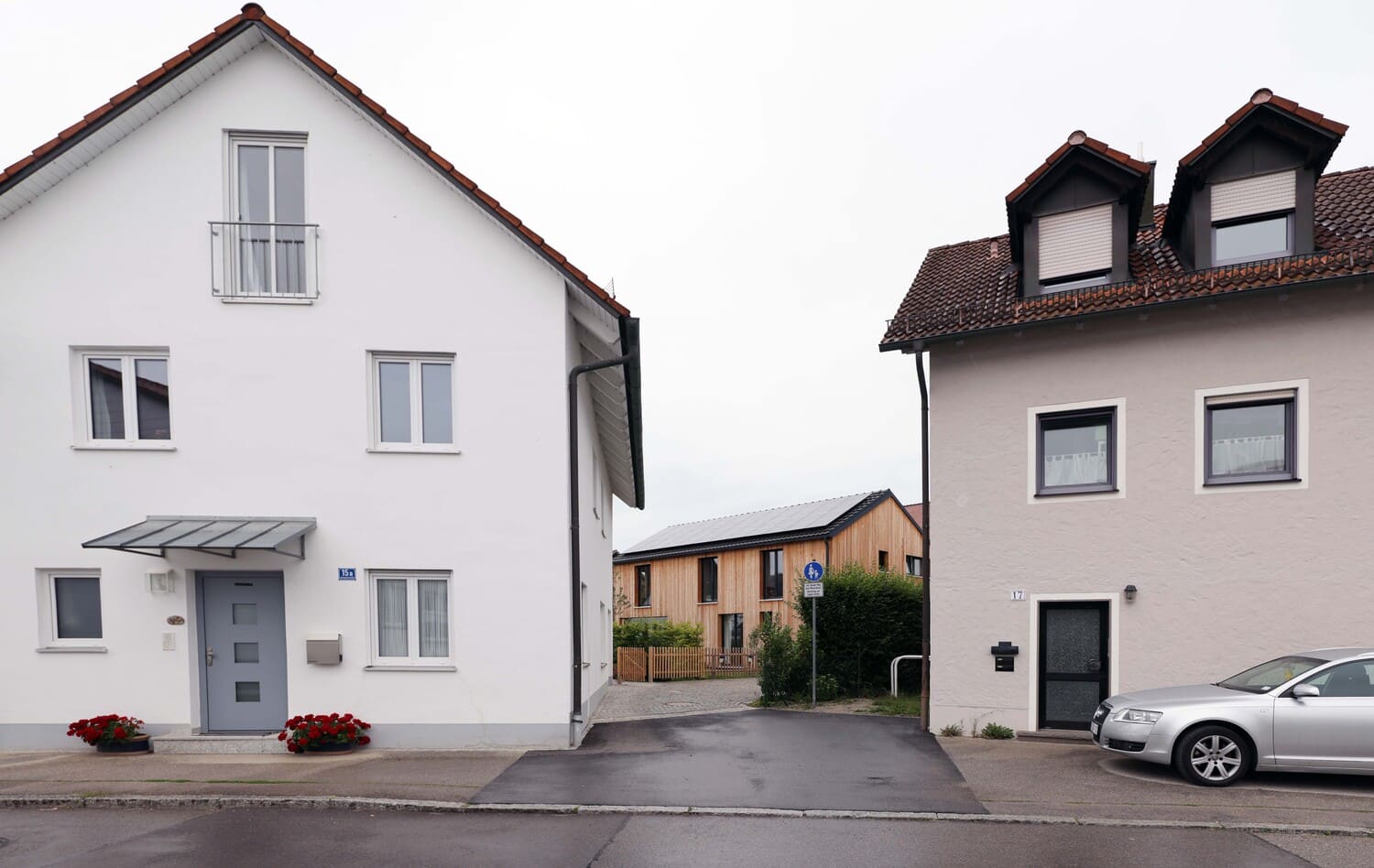 Blick auf Holzfassade vom Holzhaus zwischen zwei verputzten Häusern hindurch