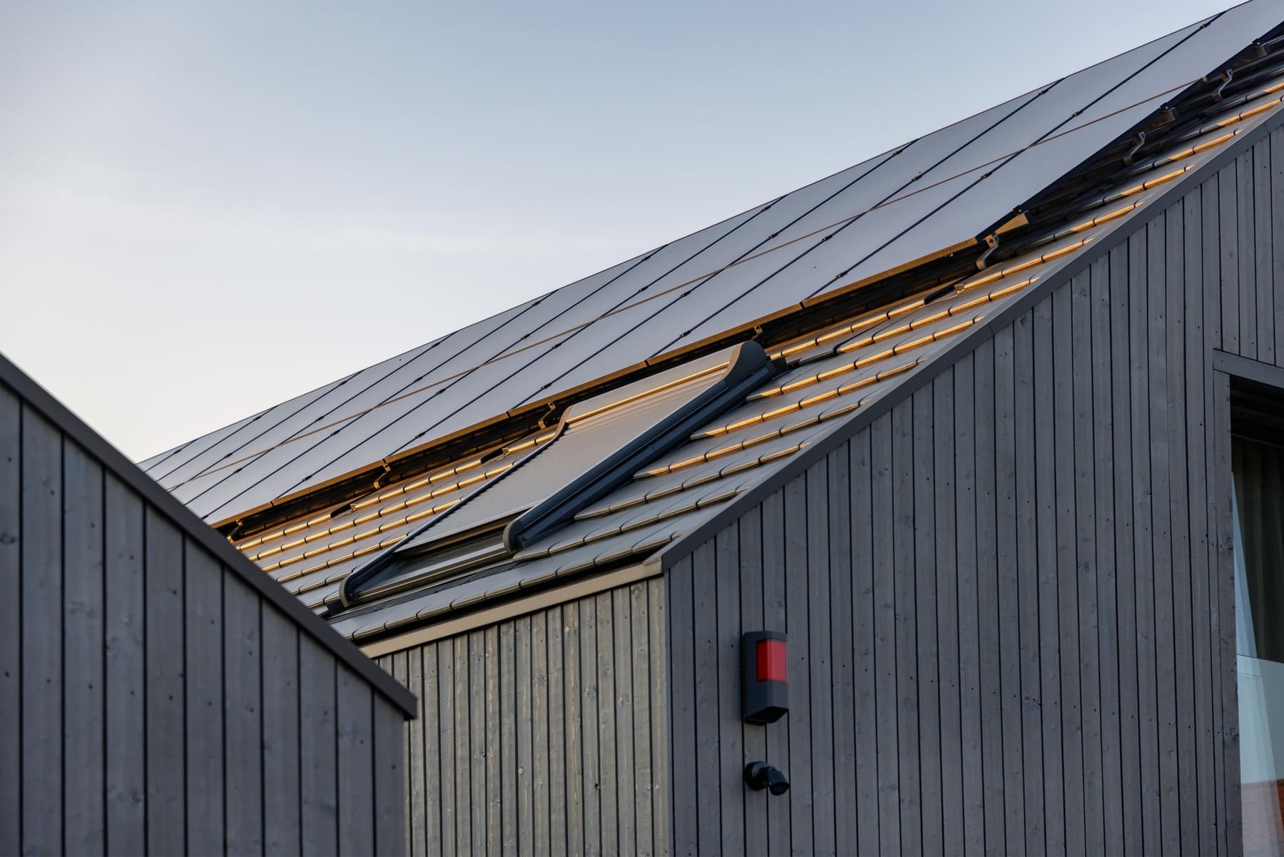Moderne Architektur mit Dachfenstern und Solarpanelen auf einem Holzhaus im sanften Licht des Sonnenuntergangs.