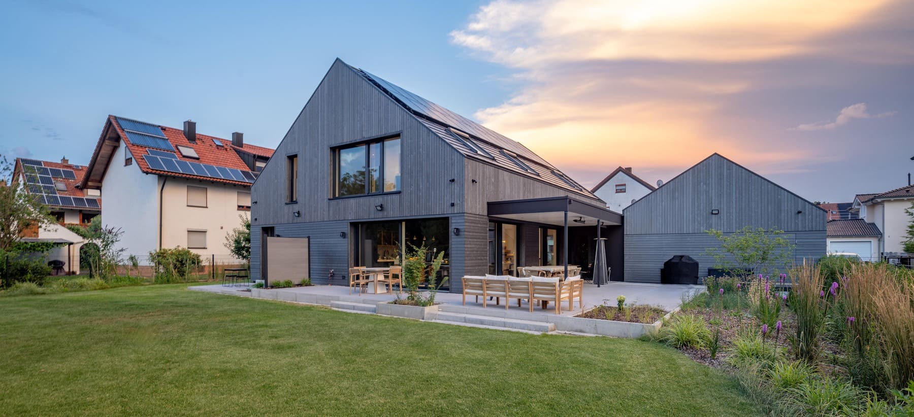 Moderne Architektur: Ein elegantes Haus mit Solarpanelen und einem schönen Garten im Abendlicht.