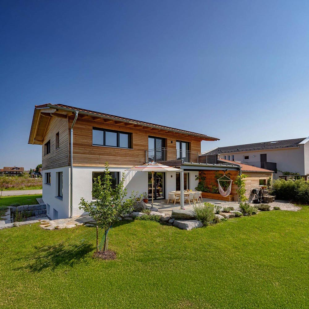 Ein modernes Einfamilienhaus in Großkarolinenfeld mit gepflegtem Garten und Sonnenterasse unter strahlend blauem Himmel.